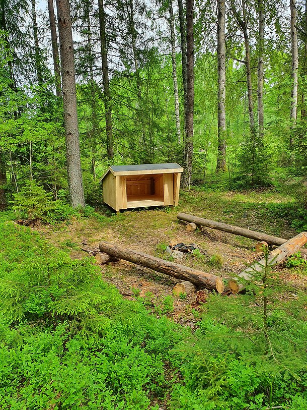 Nybyggt vindskydd med bänkar runt grillplats, i skogen vid Lockmora.